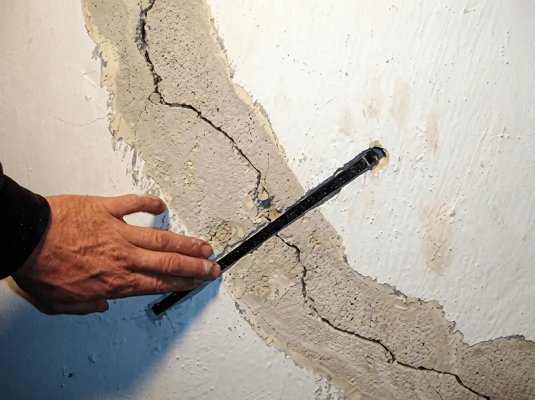 A wall with a large crack is being inspected by a professional in Houston, TX