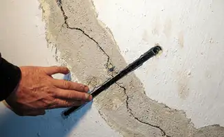 A wall with a large crack is being inspected by a professional in Houston, TX